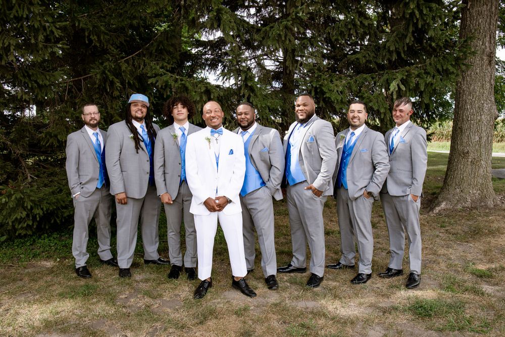 Wedding party in coordinated grey suits and blue accents posed outdoors under evergreen trees.