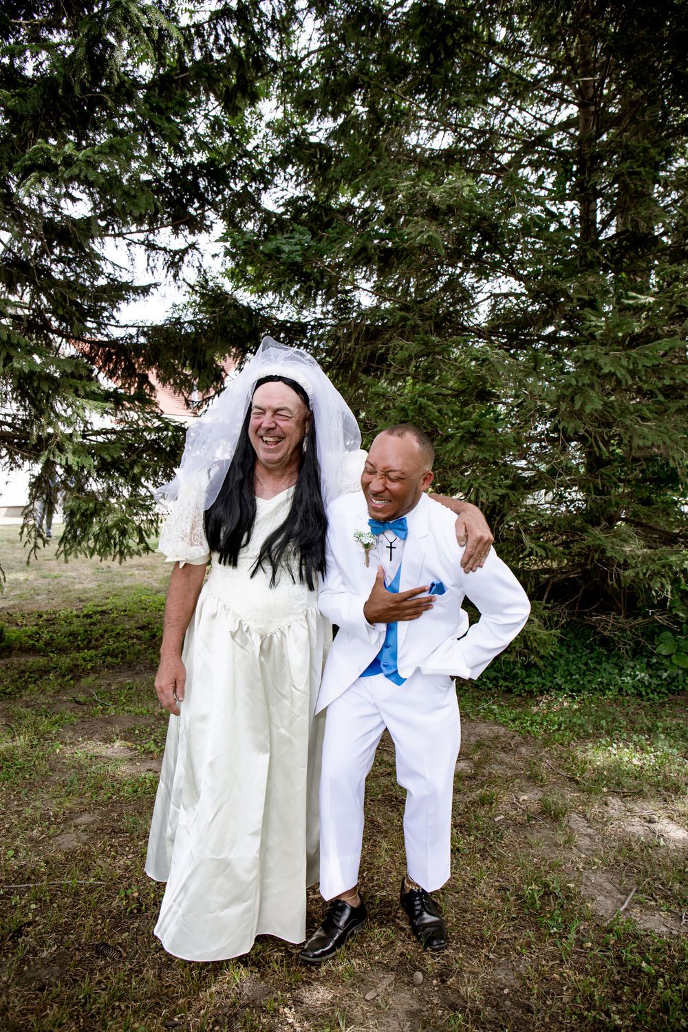 A joyful wedding moment shared between two people outdoors near pine trees.