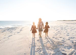Three girls, sisters, walk down the beach into the sun with the ocean on Perdido Key, FL
