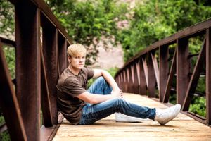 Person sitting casually on wooden bridge with natural scenery.