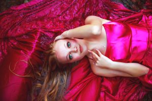 Model in flowing pink gown poses dramatically on ground.