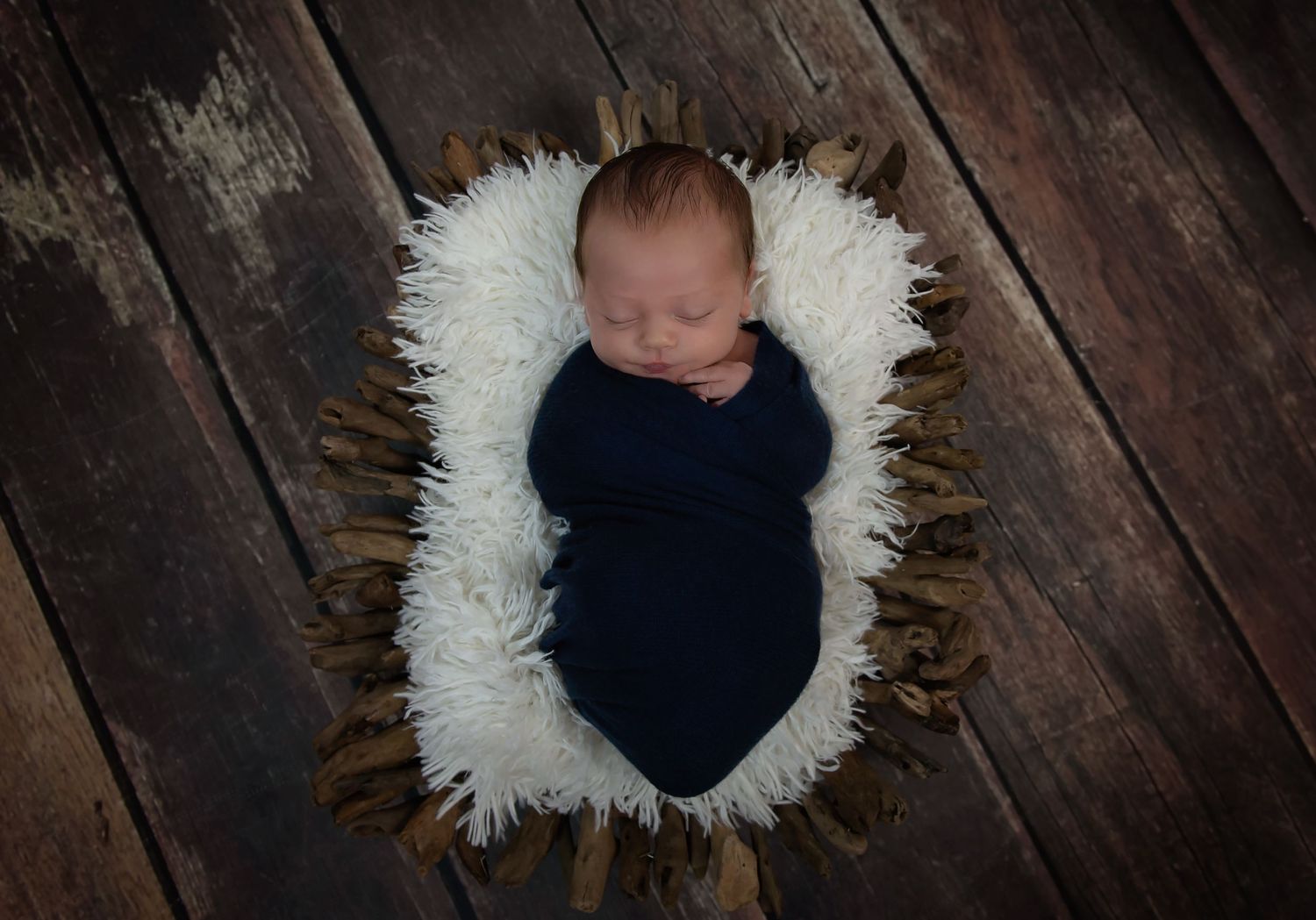 Artistic newborn photography setup with white fur circle on dark wooden floor.