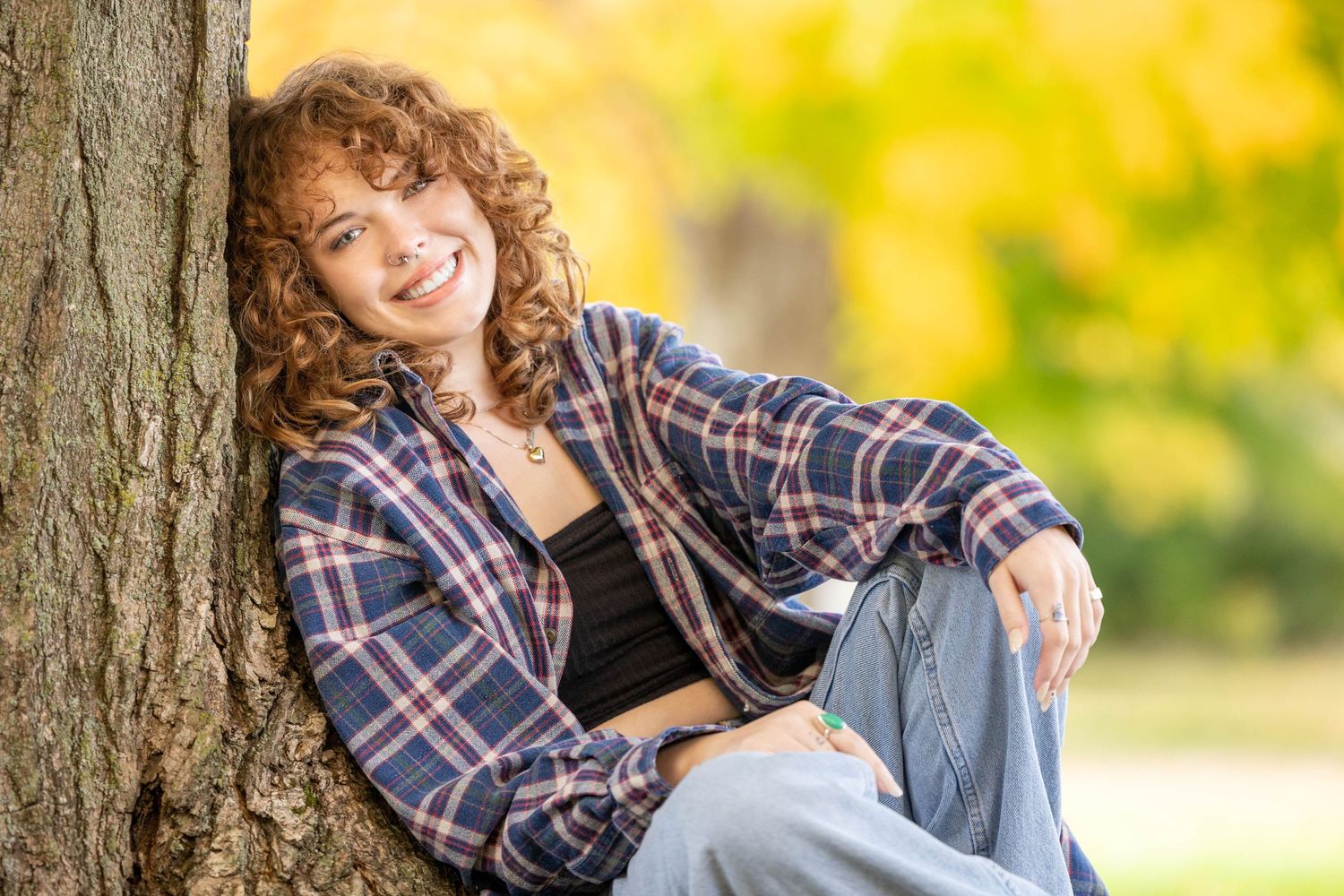 Curly haired redhead leaning against a tree in the fall
