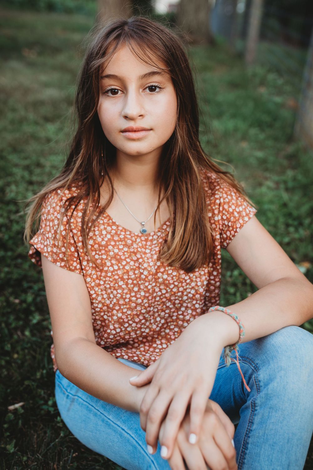 A casual portrait of someone wearing a floral top and jeans while sitting outdoors.