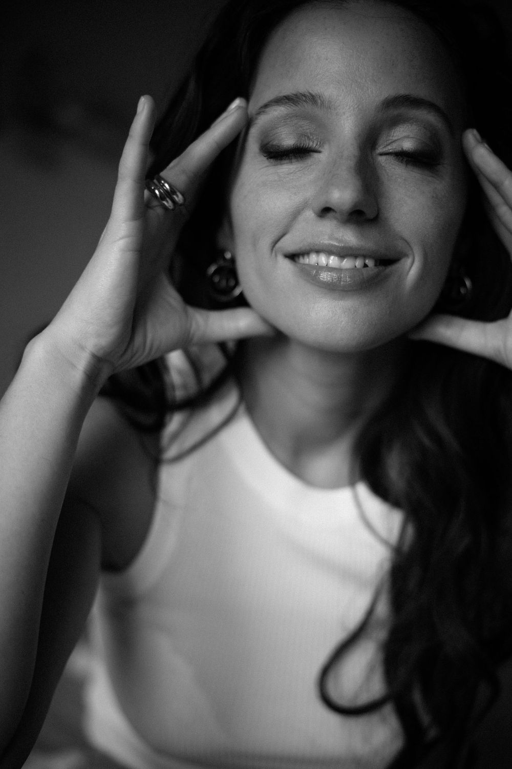Artistic black and white portrait showing peaceful expression with hands framing face.