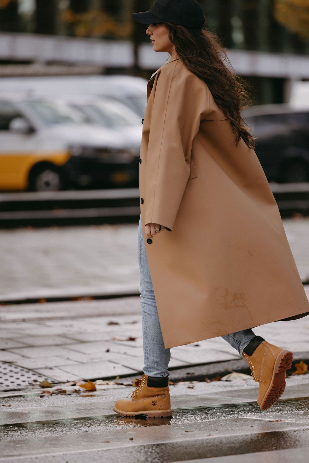 Stylish street fashion look featuring long camel coat and boots on rainy day.