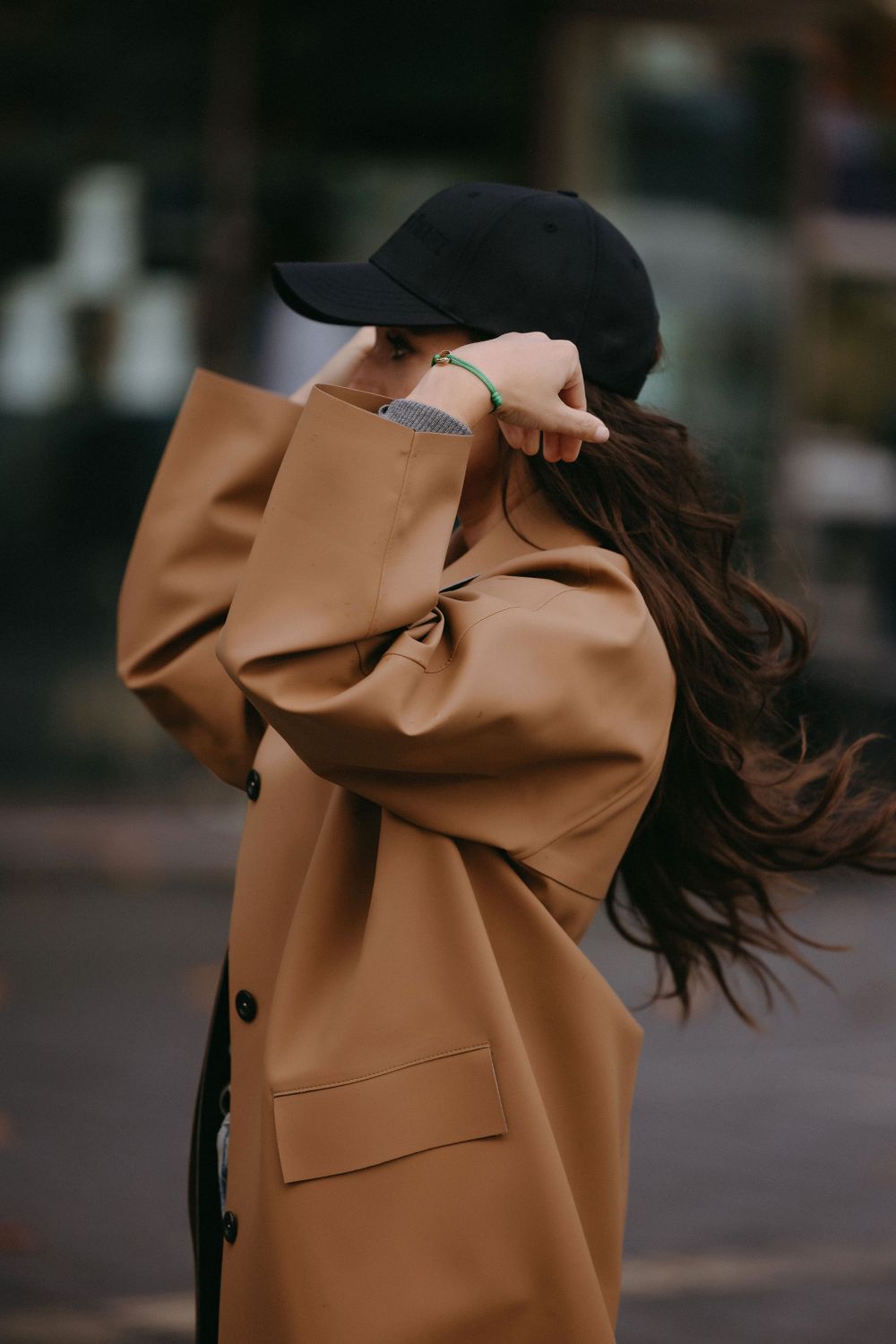 Fashion shot of camel trench coat and black baseball cap with flowing hair.