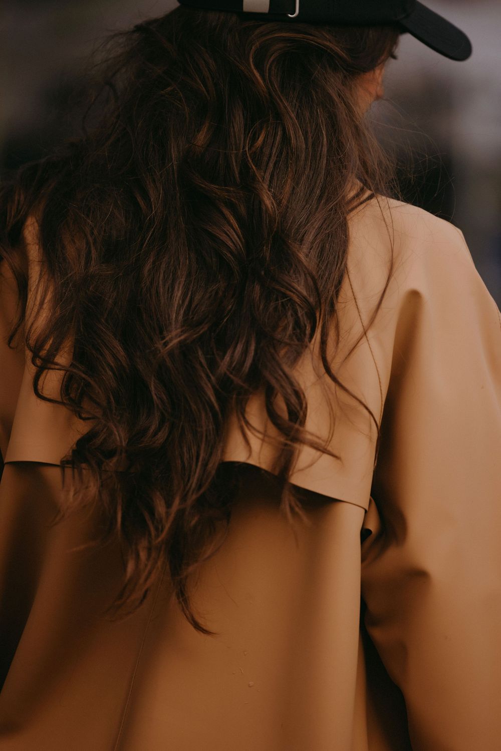 Back view of camel coat showing detailed tailoring and styling with baseball cap.