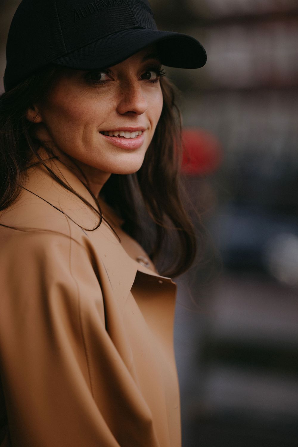 Street style portrait showcasing camel coat and casual baseball cap.