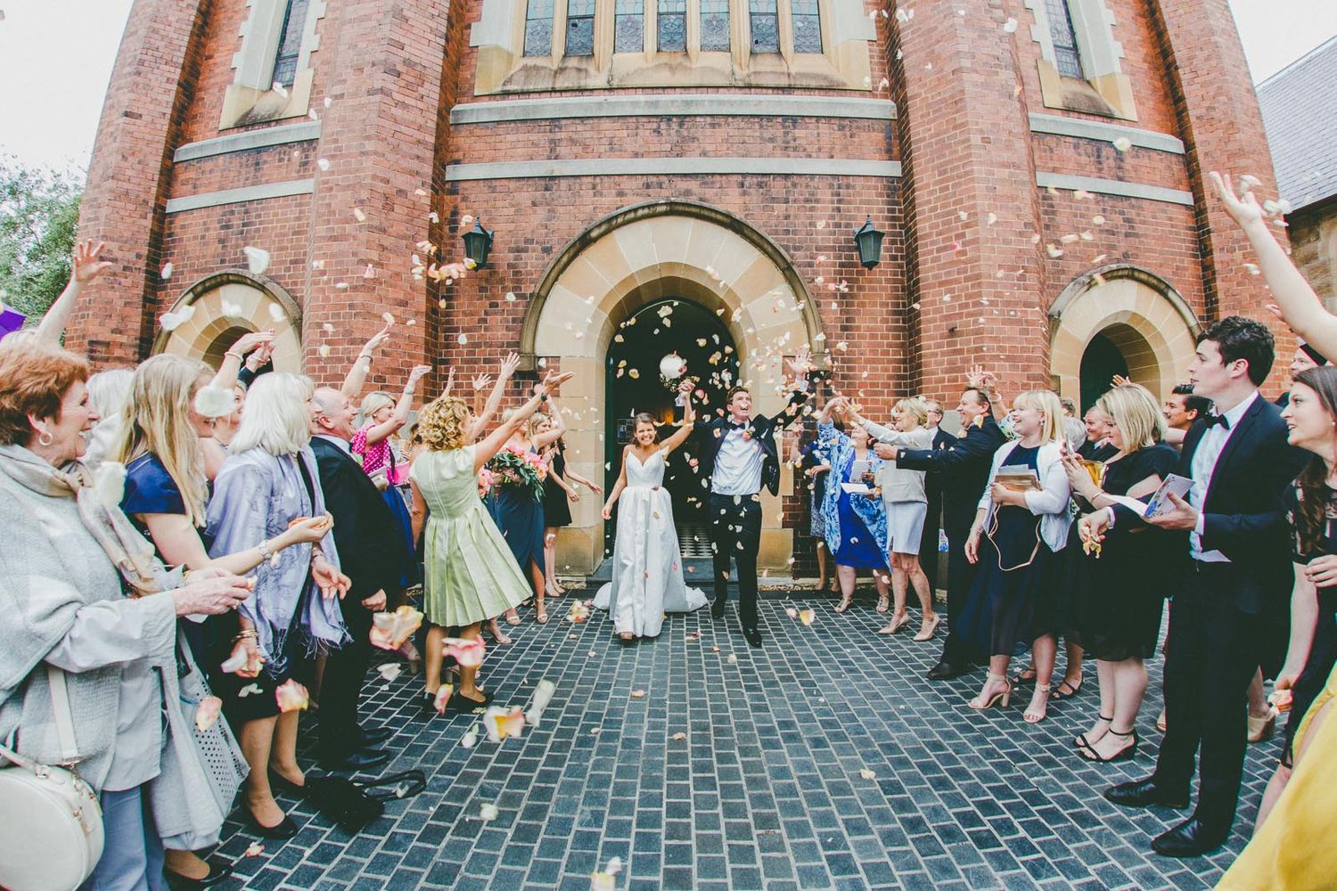 Guests cheer while wedding couple exit church