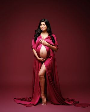 Elegant maternity portrait with flowing red silk fabric draping against dark background.