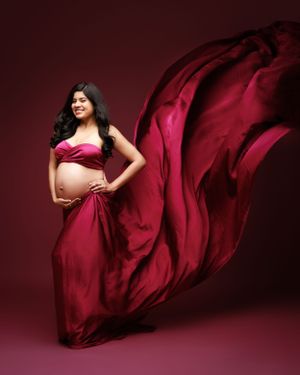 Dramatic maternity photo with billowing red silk fabric creating flowing movement.