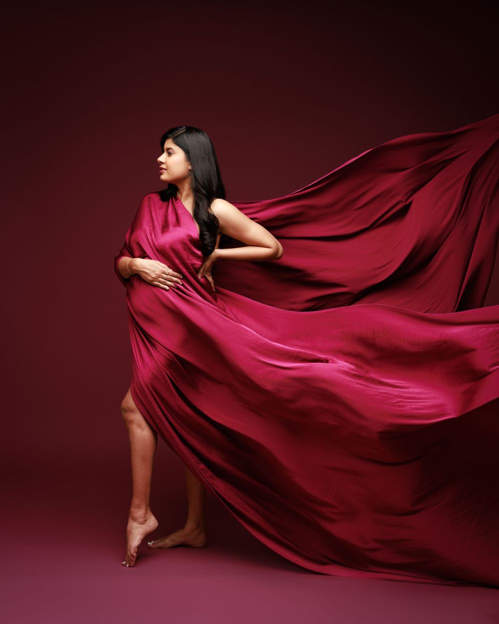 Dynamic maternity photo with flowing red fabric creating movement against burgundy background.