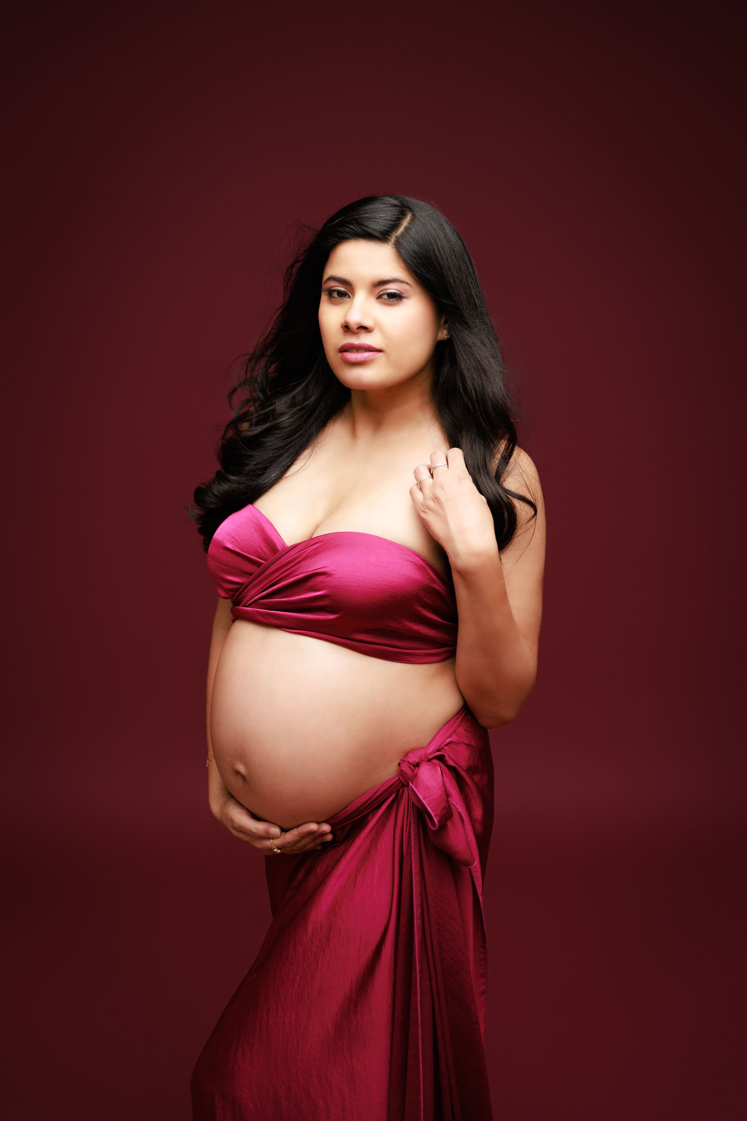 A maternity photoshoot featuring a deep red fabric wrap against a burgundy backdrop.