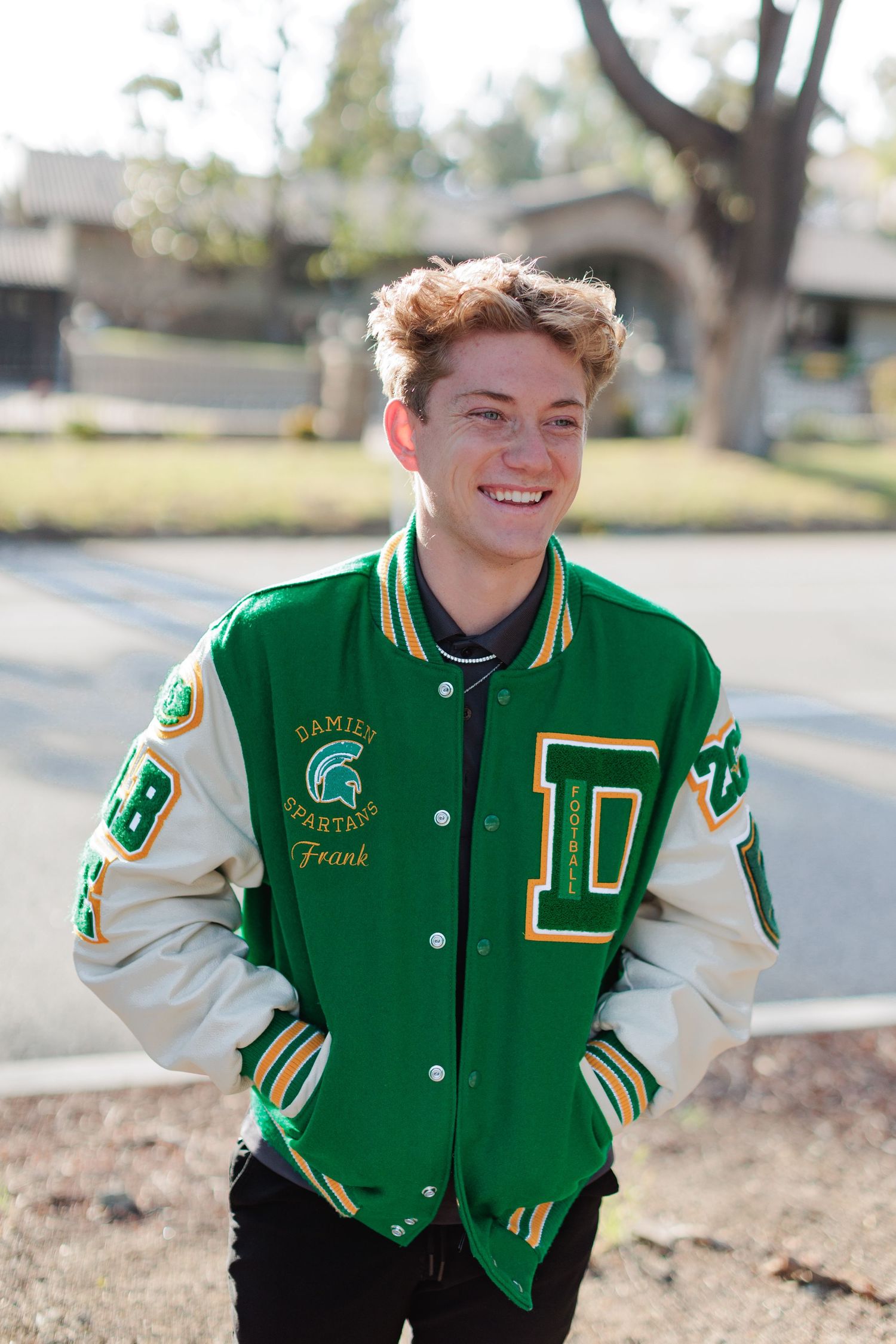 Guy in green letterman jacket smiling outside with backlight.