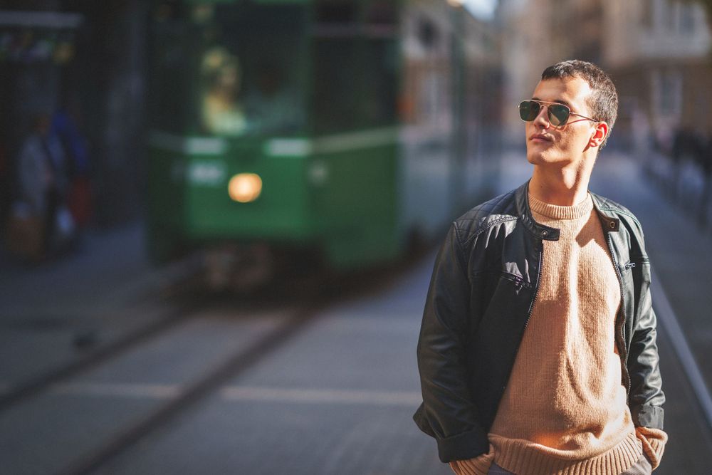 Casual street style photo with person in leather jacket and sweater near passing tram.