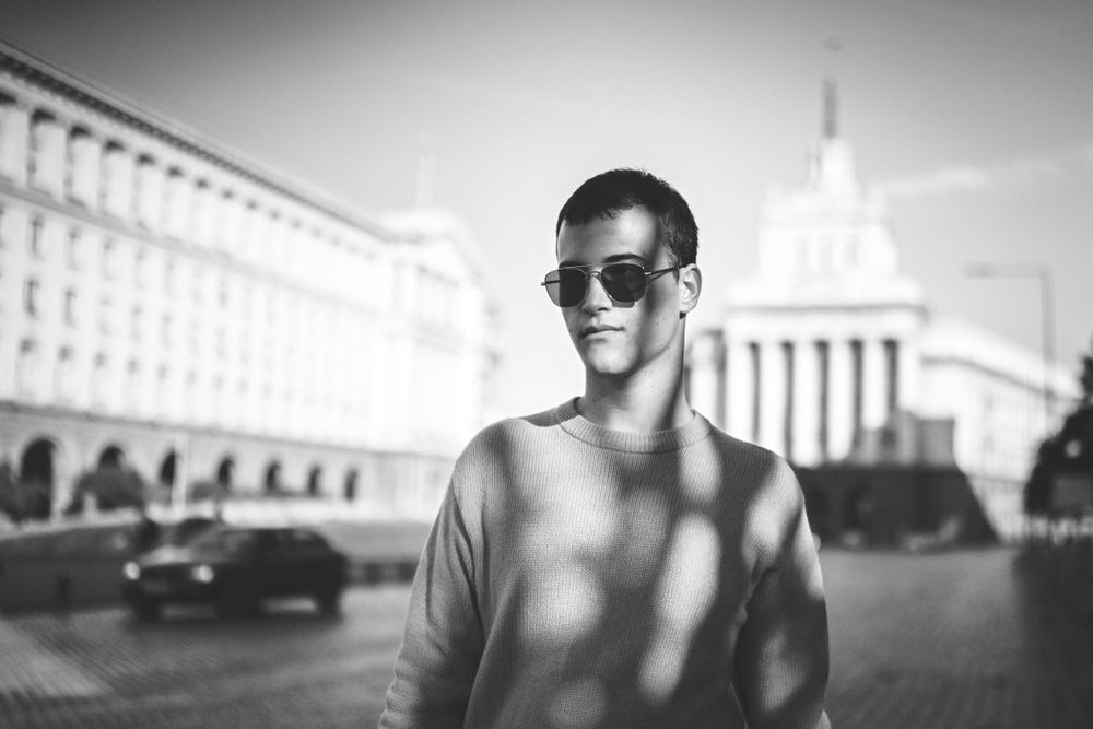 Black and white portrait of person smiling in front of architectural building.
