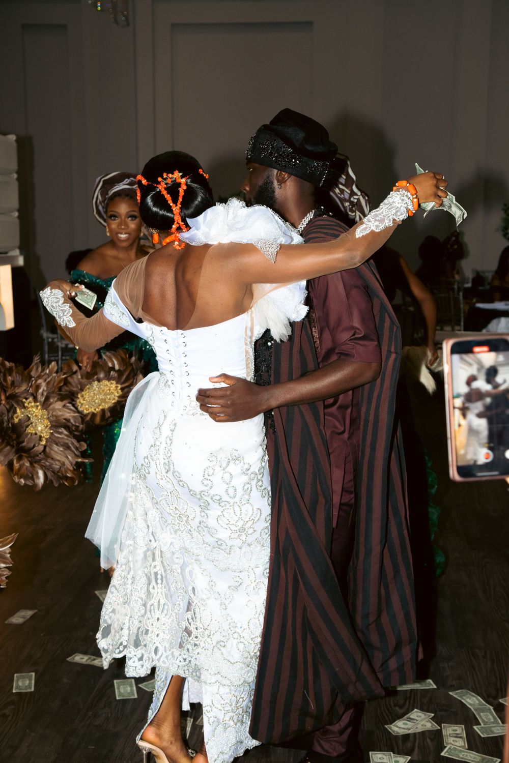 A couple dances together at a celebration, with the woman wearing an elegant white lace dress and the man in a striped robe.
