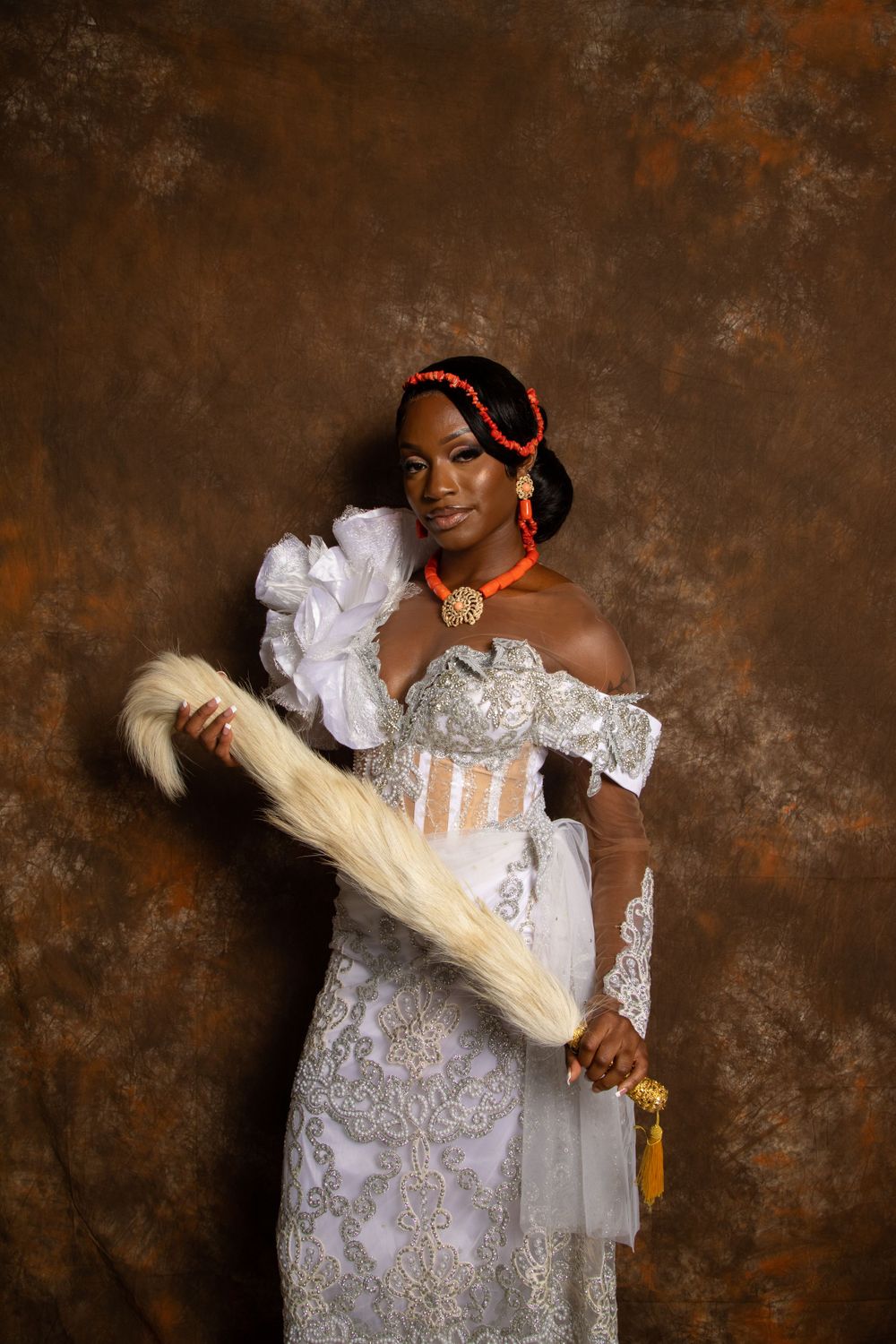 Elegant portrait of woman in white lace gown holding decorative fan against textured backdrop.
