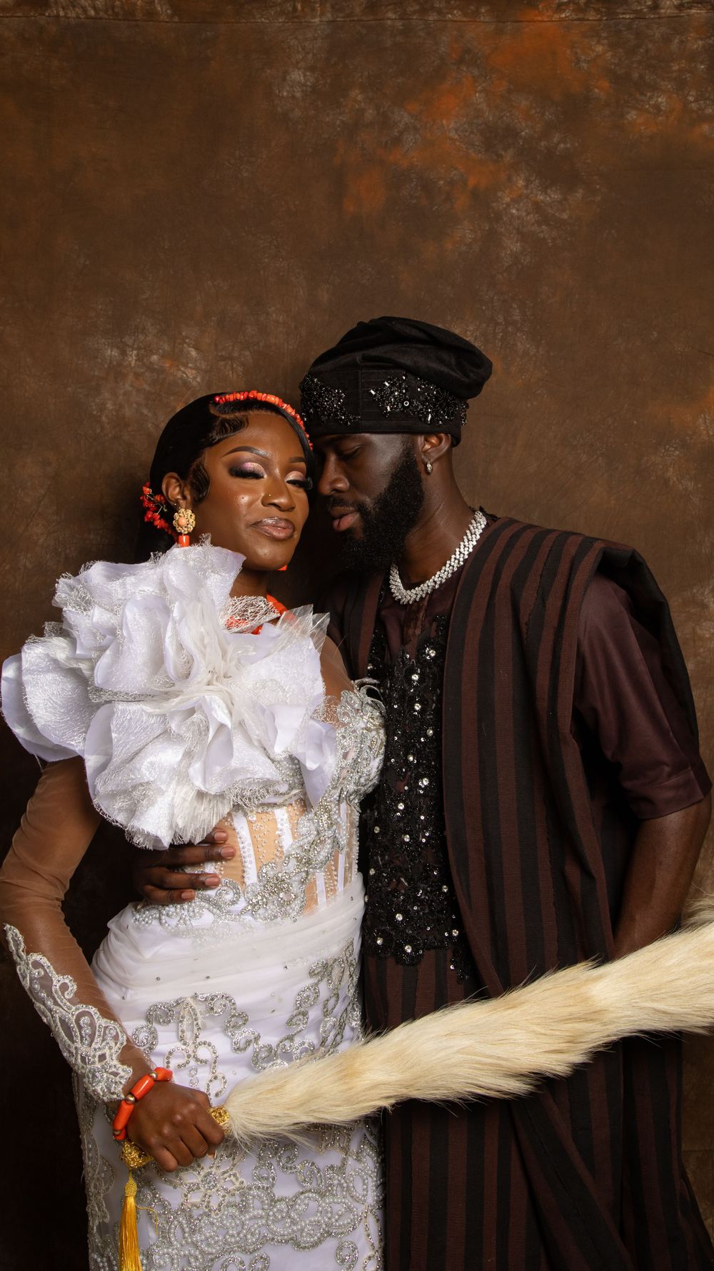 Intimate portrait of couple in traditional attire against textured brown background.