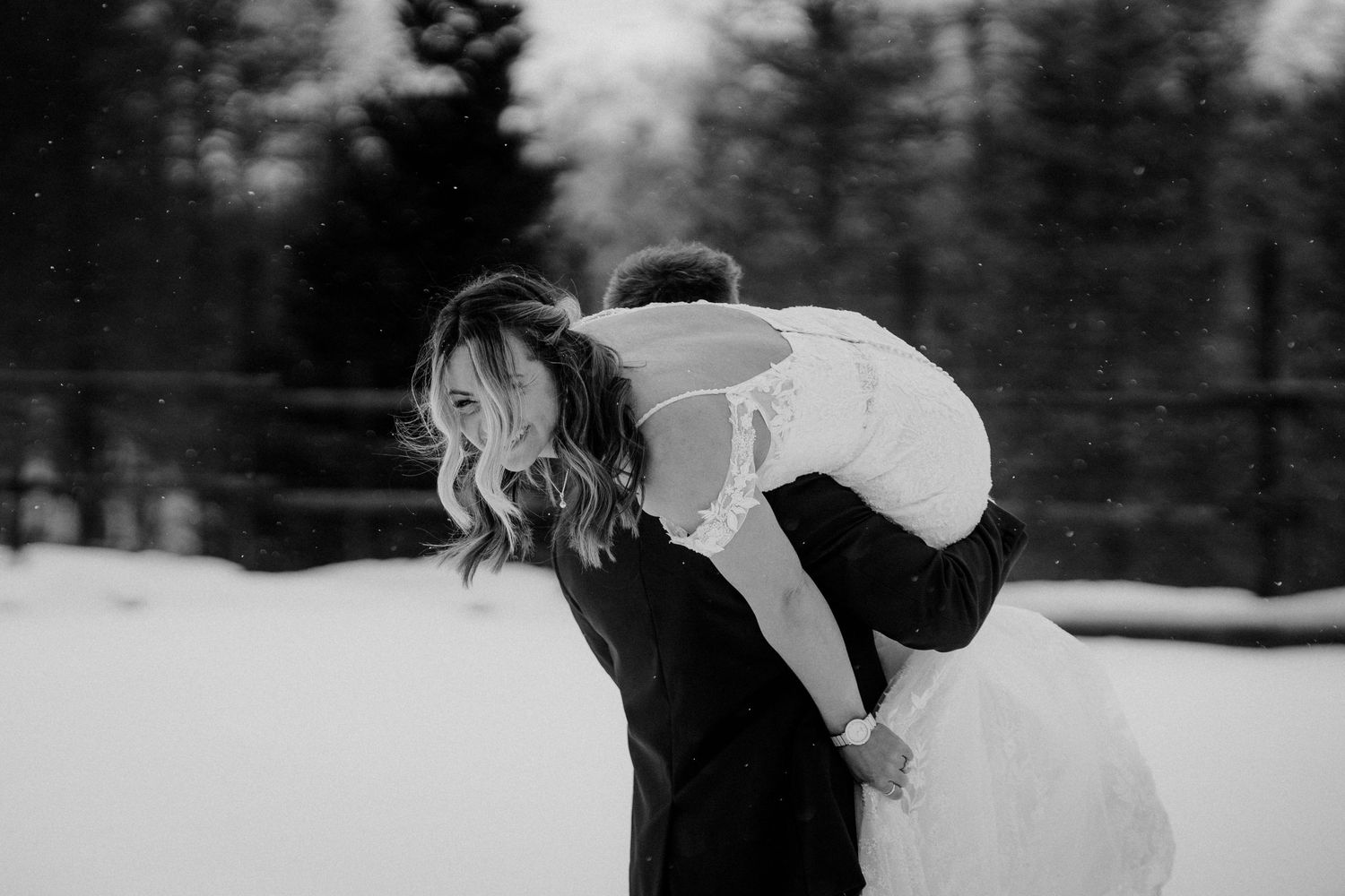 Black and white photo of playful wedding couple having fun in a snowy winter landscape.
