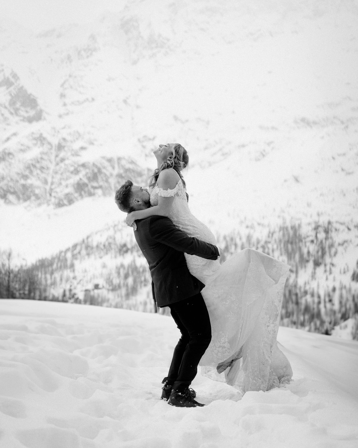 Couple in wedding attire sharing a joyful lift pose against snowy mountain backdrop.