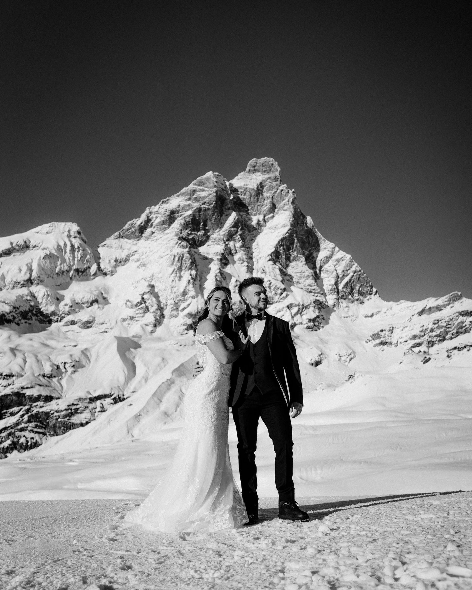 A black and white wedding portrait with dramatic mountain peaks in background.