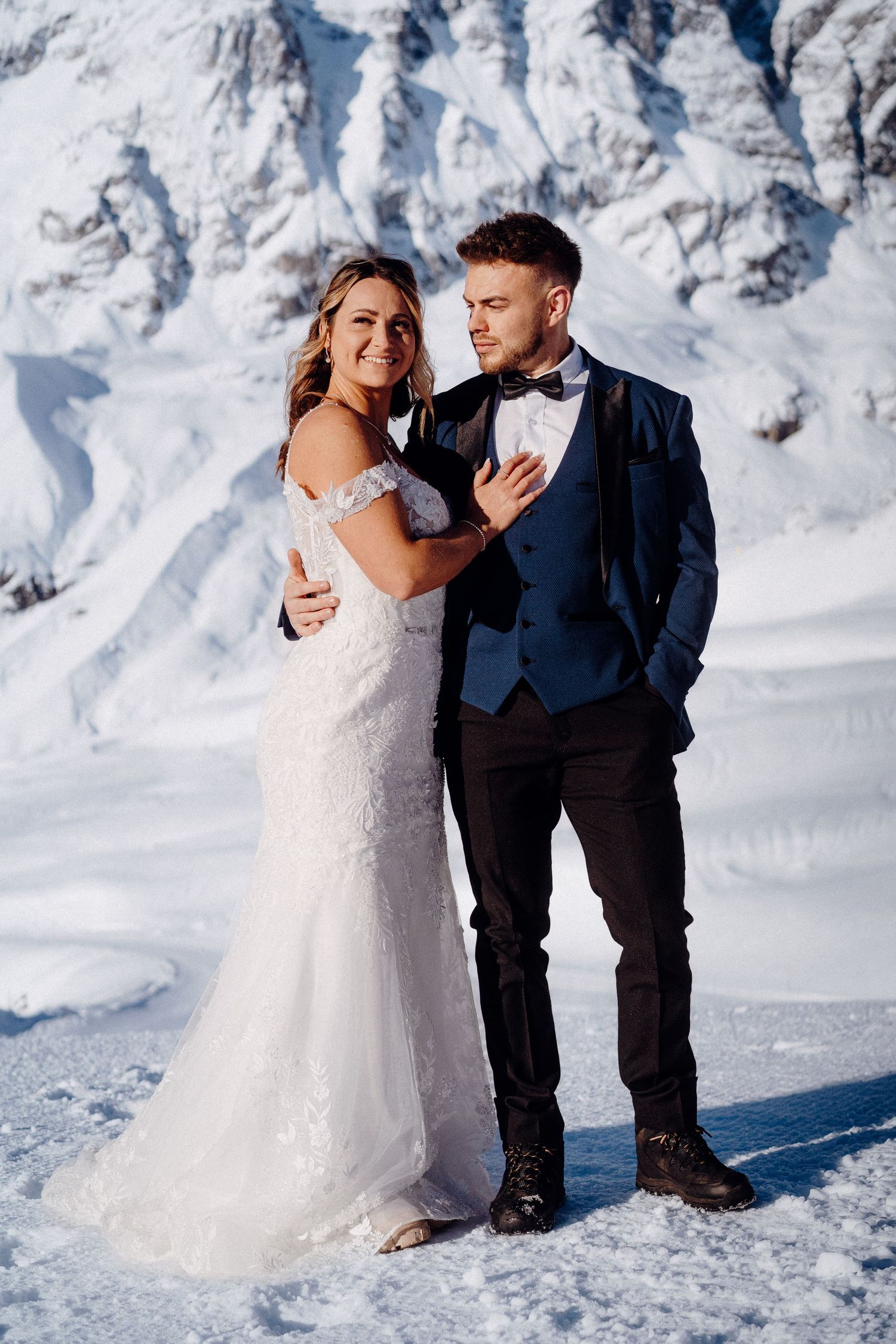 A couple in wedding attire embraces on a snowy mountain slope.