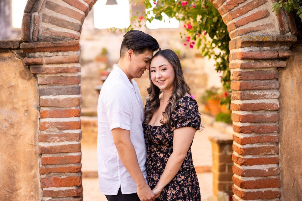Couple sharing intimate moment under brick archway with Mediterranean garden backdrop.