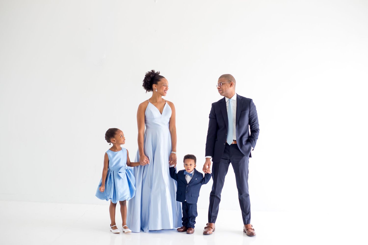 formal studio family photoshoot session family wearing blue satin dress with dad wearing a black suit all white studio