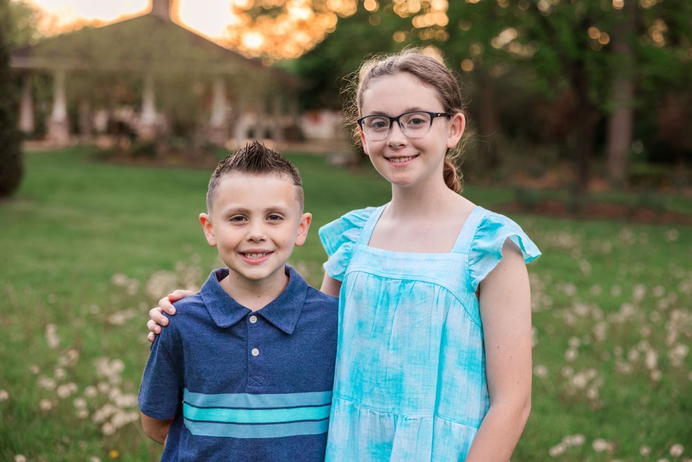 Two young people in blue outfits standing together on a lawn at sunset.