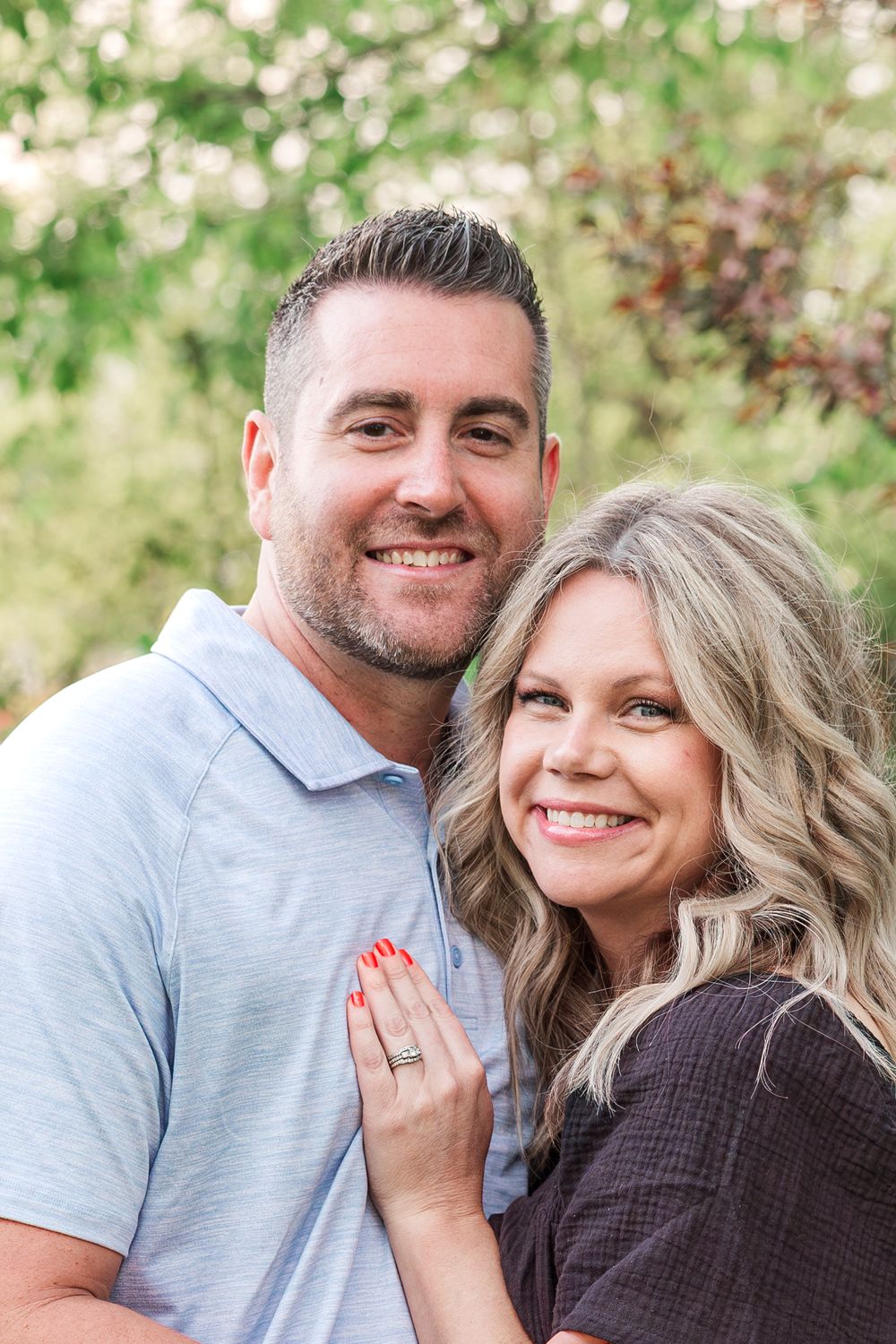 Couple poses together outdoors with flowering trees and natural landscaping in background.