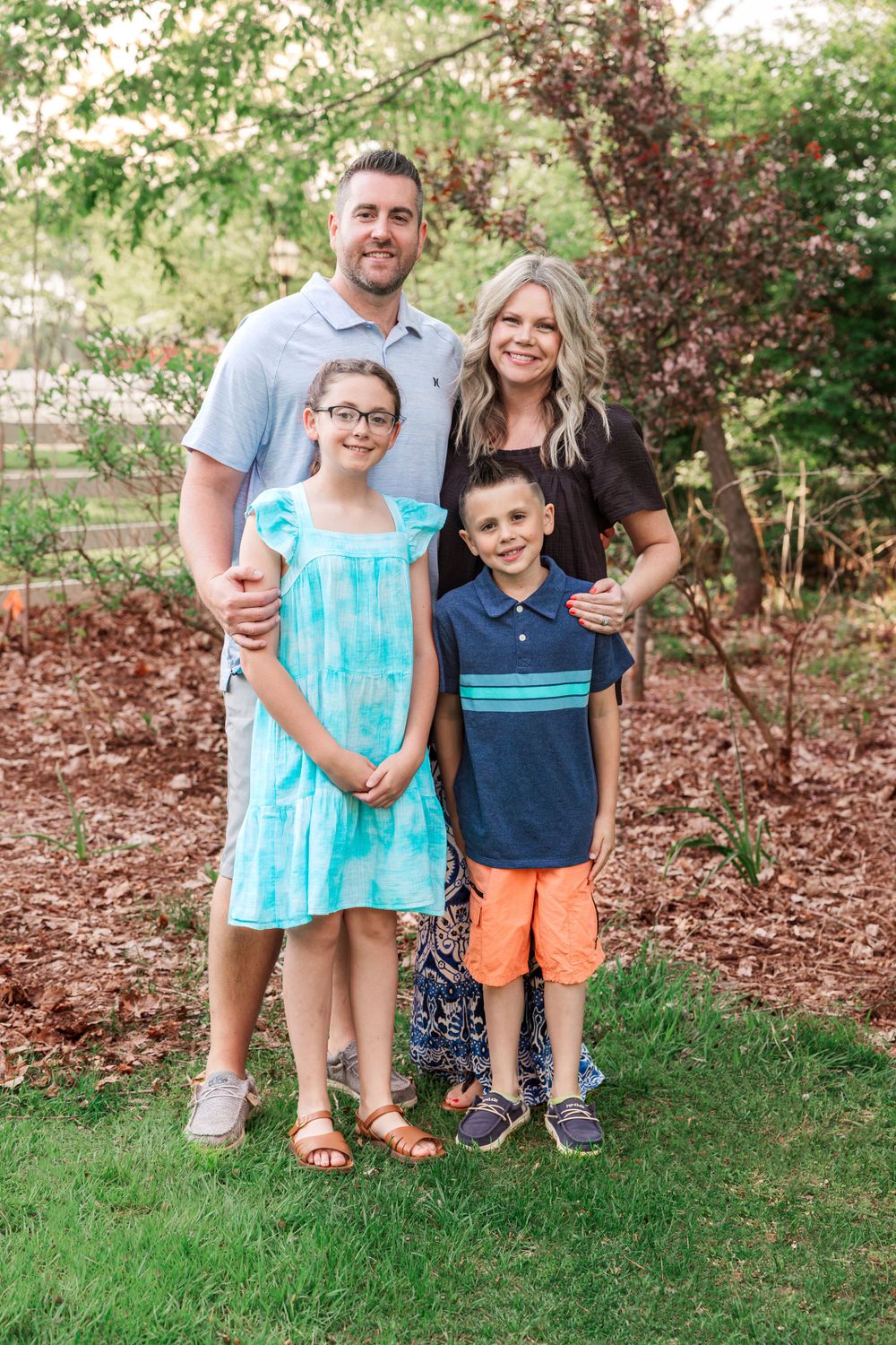 Family of four poses together in front of flowering trees and natural landscaping.