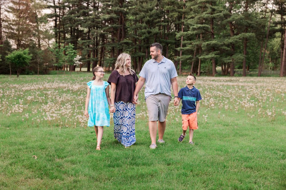 Family walking together across a grassy field with pine trees in the background on a sunny day.