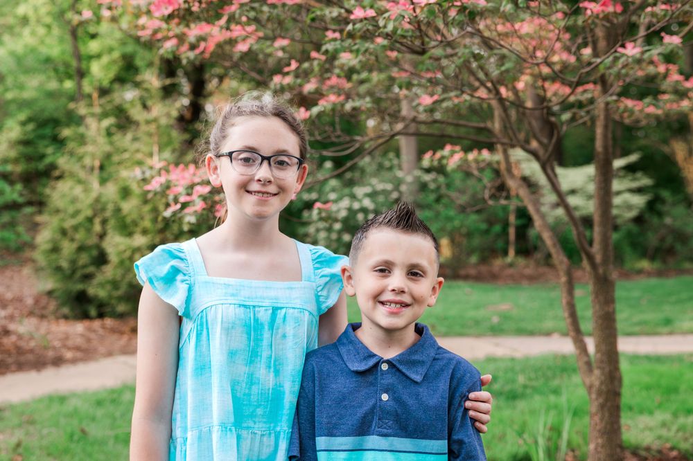 Two young siblings in coordinating blue outfits pose together in garden setting.