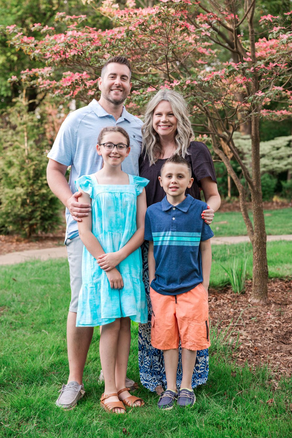 Family portrait in garden setting with blooming pink dogwood trees in background.