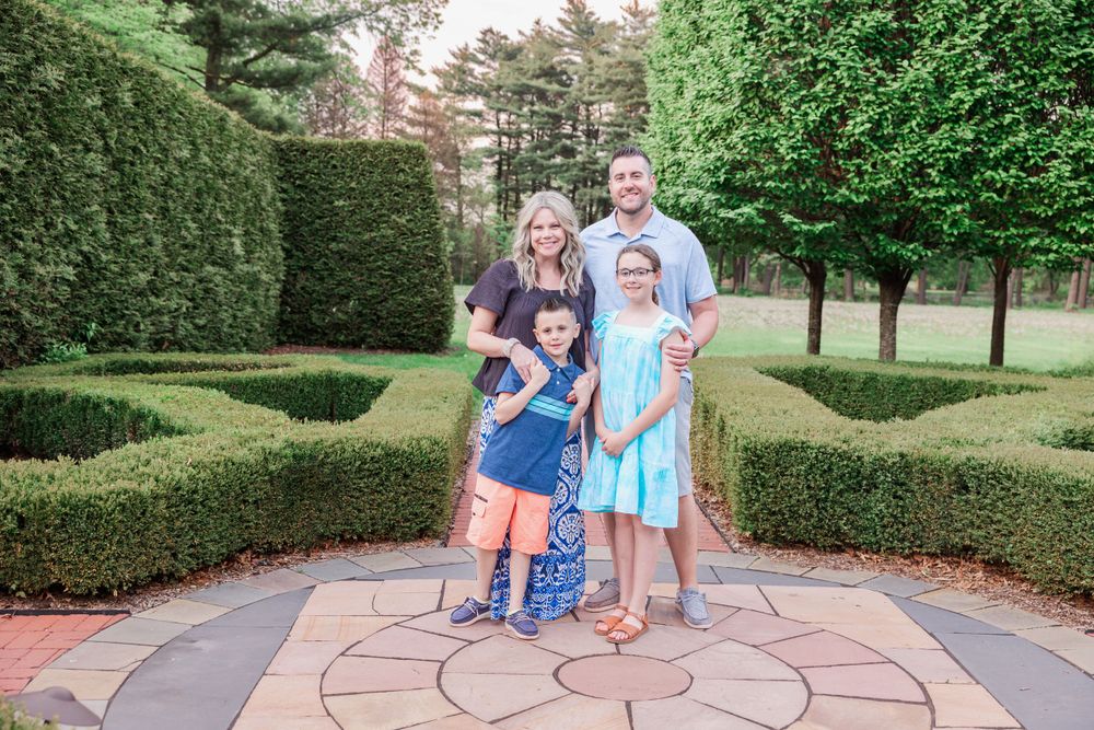 Family group poses on decorative stone patio surrounded by manicured hedges.