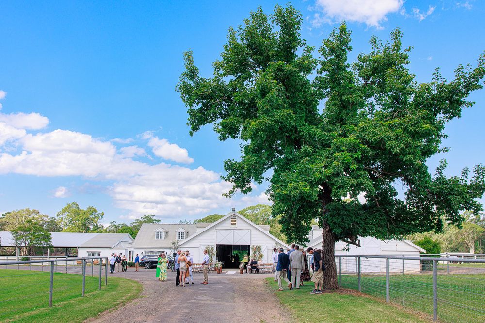 Panoramic view of a rustic farm venue with white buildings and green fields under blue skies.