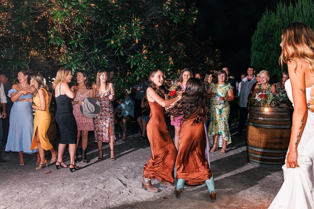 Wedding party and guests dancing on outdoor patio during evening celebration.