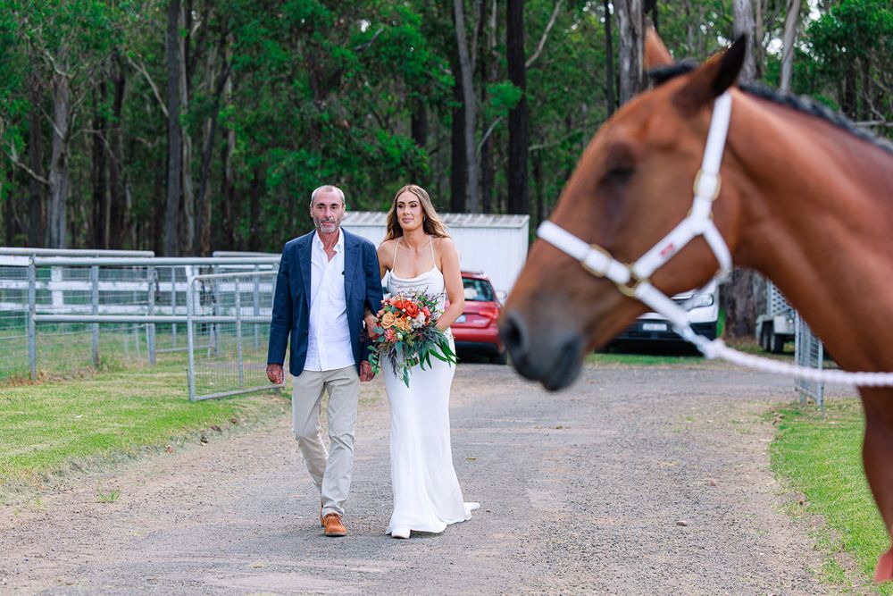 Wedding party poses for photos with a horse at an outdoor venue with white fencing.