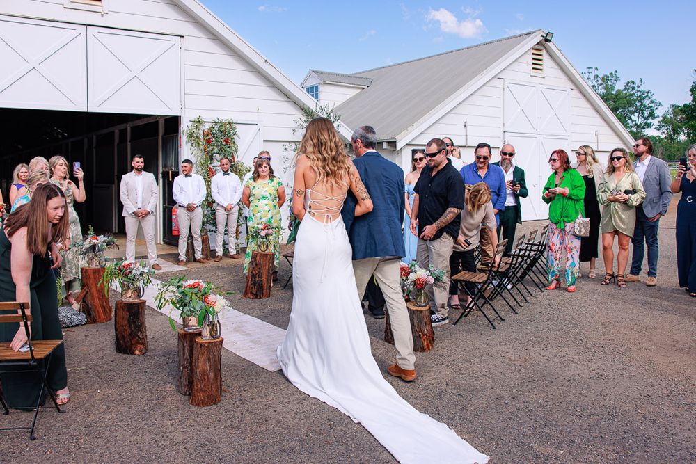 Wedding guests gather outside white barn venue for celebration.