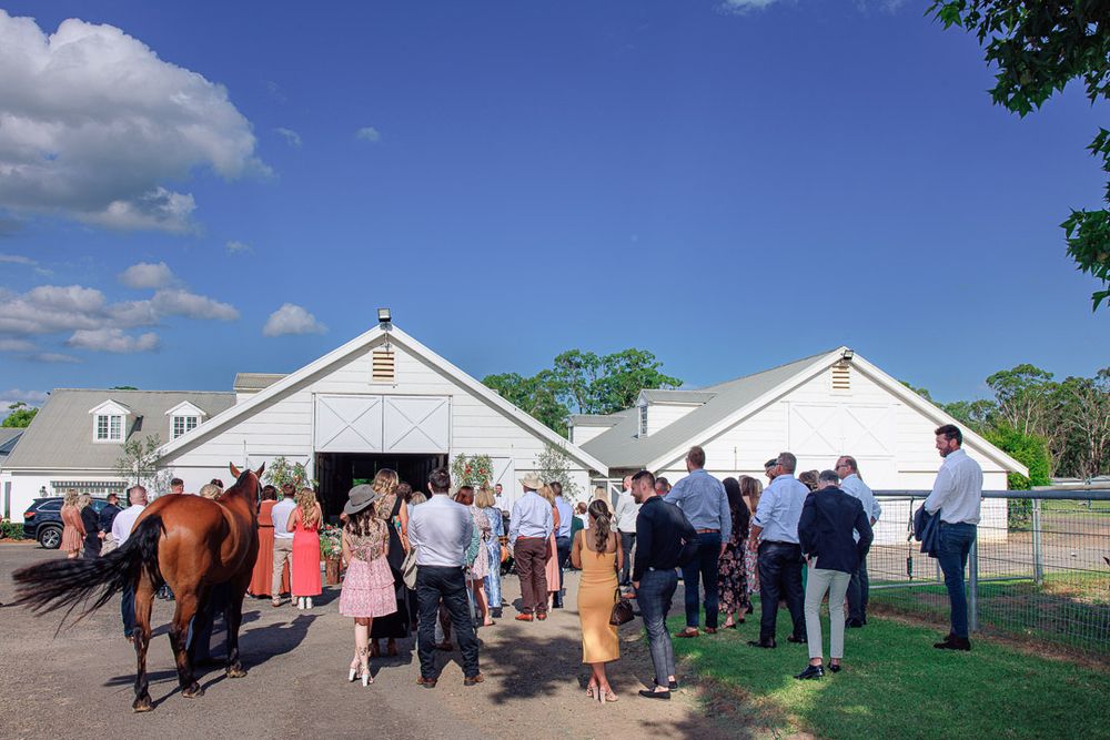 Outdoor wedding gathering at white barn venue under blue sky.