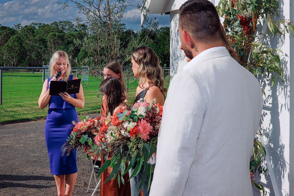 Outdoor wedding ceremony setup with floral arrangements against white barn backdrop.