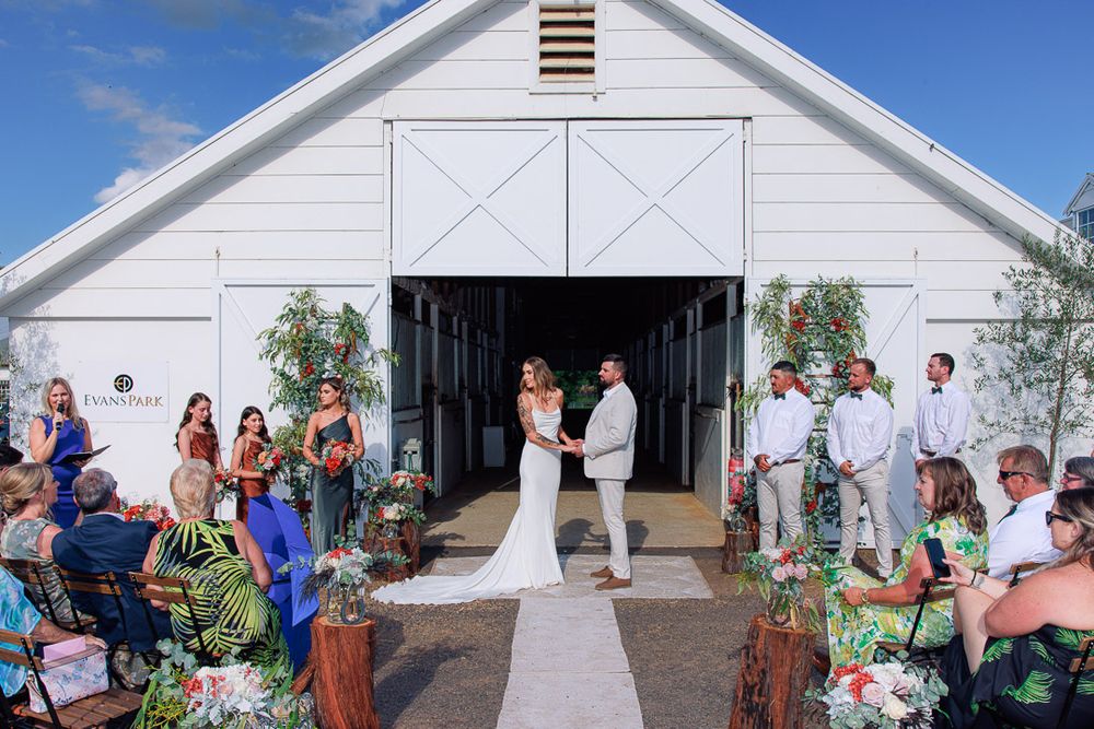 Guests gather for outdoor celebrations in front of a rustic white barn building.