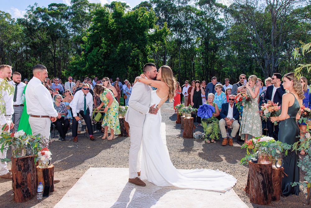 Wedding guests seated outdoors for ceremony with natural wooded backdrop.