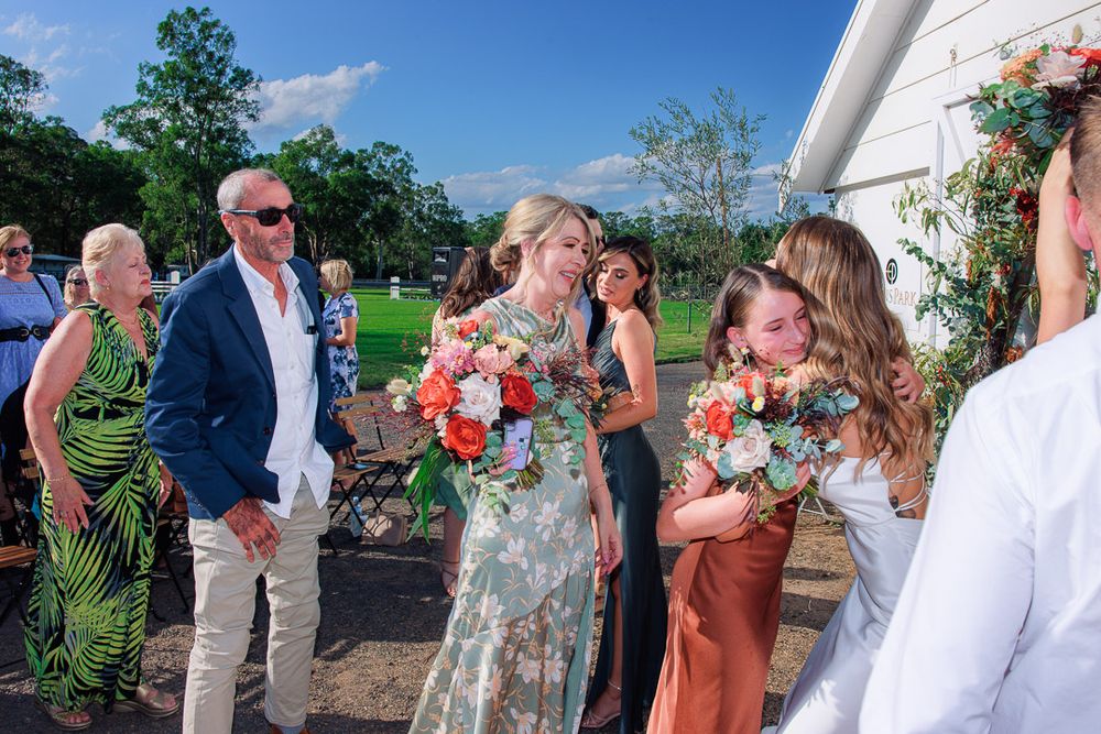 Wedding party and guests mingle during outdoor reception at barn venue.