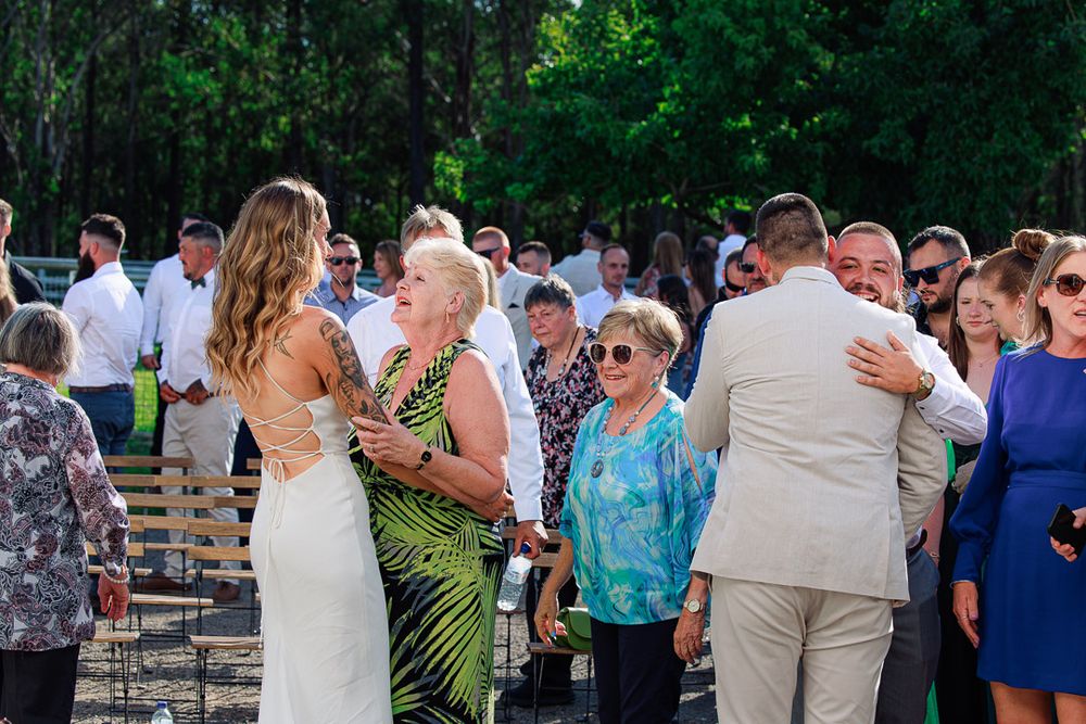 Guests celebrate during outdoor wedding reception with trees in background.