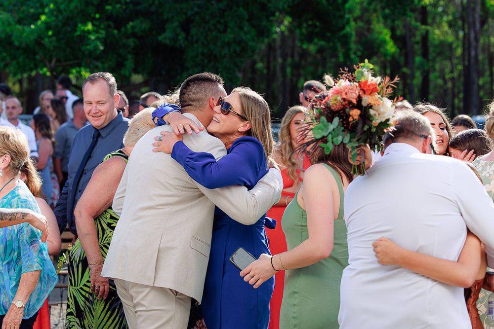 Wedding party members share embraces during outdoor celebration.