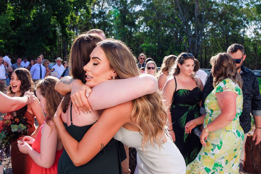 Wedding guests share emotional embraces during outdoor celebration.