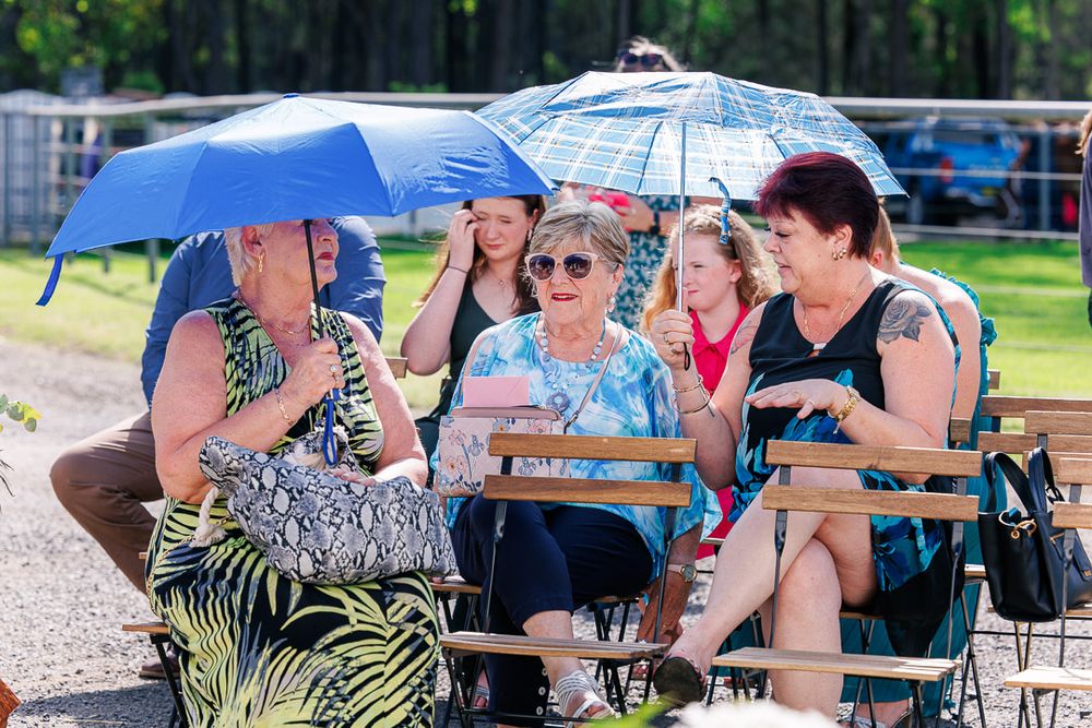 Wedding guests enjoying outdoor reception under blue umbrellas on a sunny day.